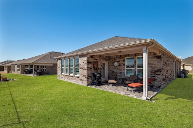 rear view of house featuring a patio area, brick siding, roof with shingles, and a lawn