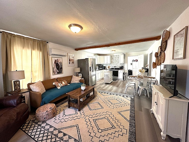 living area with a textured ceiling, an AC wall unit, wood finished floors, and a healthy amount of sunlight