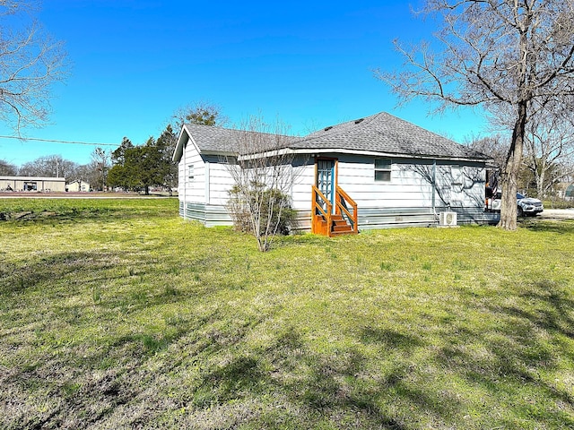 rear view of property with a lawn, entry steps, and a shingled roof