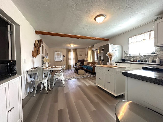 kitchen featuring stainless steel refrigerator with ice dispenser, tasteful backsplash, open floor plan, dark wood finished floors, and white cabinetry