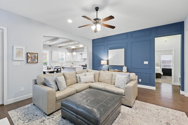 living room featuring arched walkways, wood finished floors, a ceiling fan, and a decorative wall