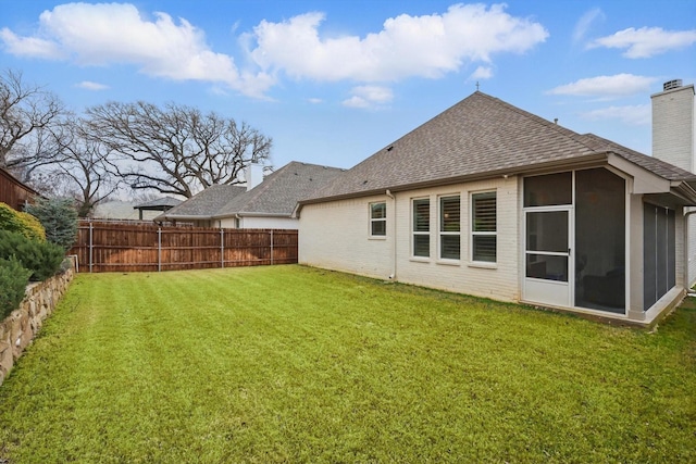 rear view of house with a lawn, a fenced backyard, roof with shingles, brick siding, and a chimney