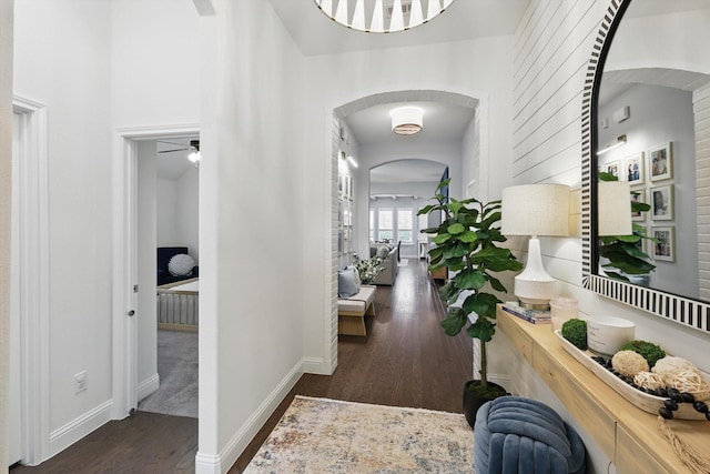 hall featuring arched walkways, baseboards, and wood finished floors