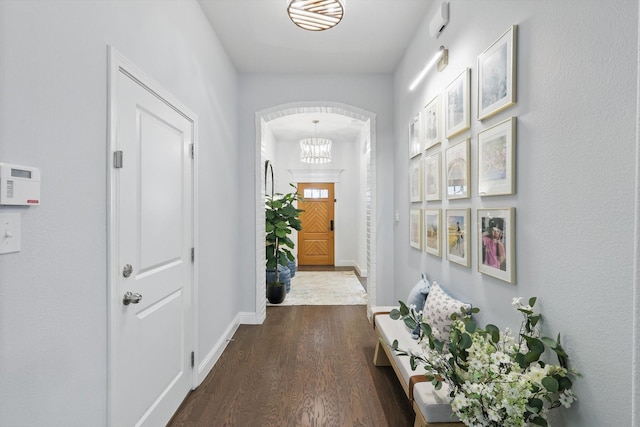 hall with dark wood-type flooring, a notable chandelier, and baseboards