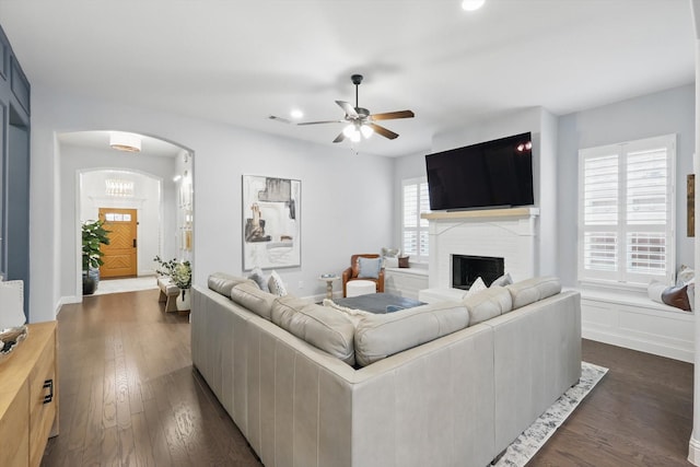 living room with visible vents, a fireplace, arched walkways, ceiling fan, and dark wood-type flooring