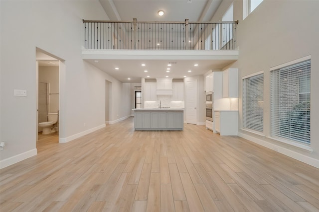 unfurnished living room featuring baseboards, a high ceiling, light wood-style floors, and a sink