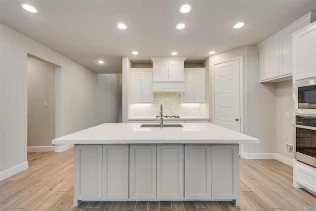 kitchen with light wood finished floors, stainless steel appliances, decorative backsplash, light countertops, and a sink