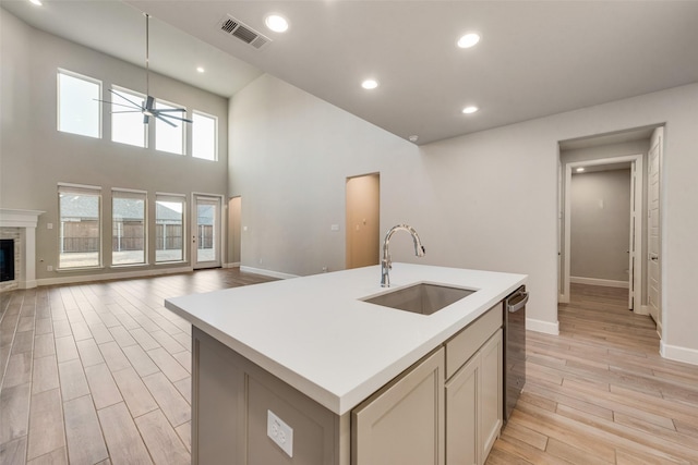 kitchen featuring visible vents, a sink, light wood-style floors, a glass covered fireplace, and open floor plan