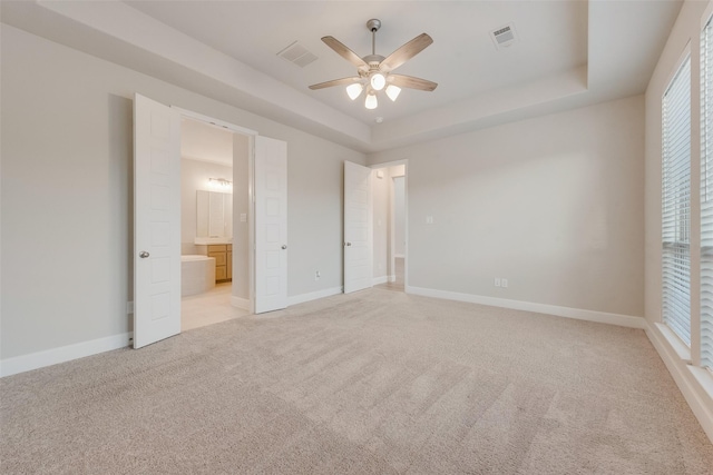 unfurnished bedroom with a raised ceiling, baseboards, visible vents, and light carpet