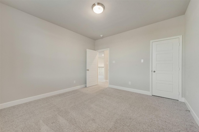 spare room featuring light colored carpet and baseboards