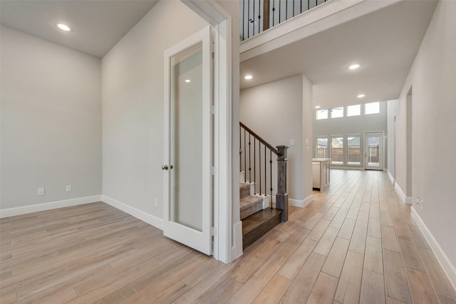 corridor with baseboards, stairway, recessed lighting, light wood-style floors, and a towering ceiling