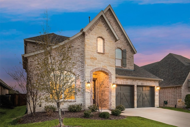 french country style house featuring roof with shingles, an attached garage, concrete driveway, stone siding, and brick siding