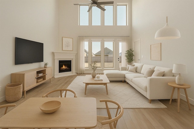living area featuring plenty of natural light, a ceiling fan, a warm lit fireplace, and light wood-style floors