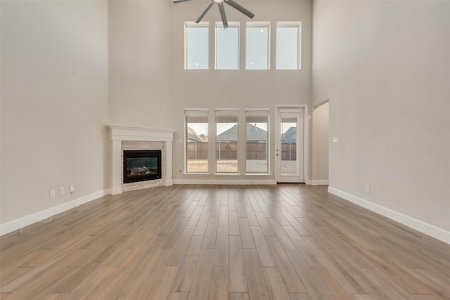 unfurnished living room with a stone fireplace, a healthy amount of sunlight, baseboards, and wood finished floors