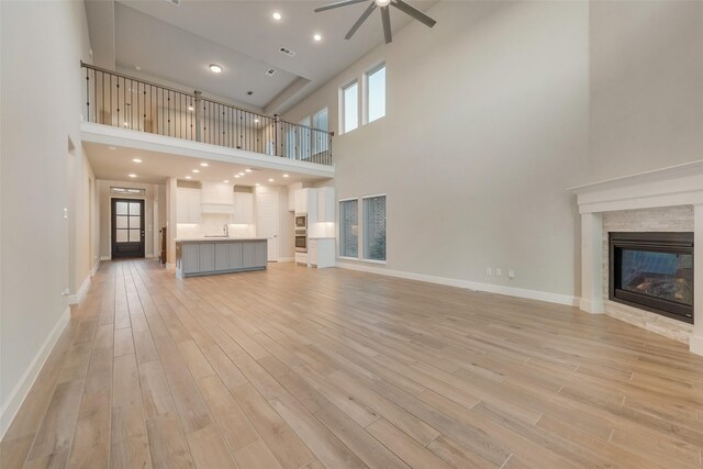 unfurnished living room with light wood-type flooring, a glass covered fireplace, a ceiling fan, and a towering ceiling