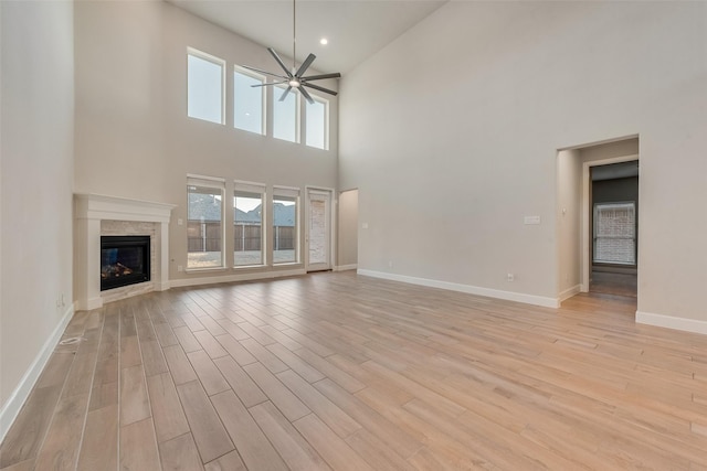 unfurnished living room featuring plenty of natural light, light wood-type flooring, a ceiling fan, and a glass covered fireplace