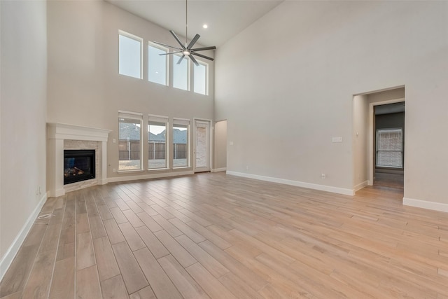 unfurnished living room with light wood finished floors, baseboards, a towering ceiling, a glass covered fireplace, and ceiling fan