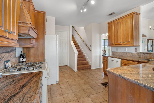 kitchen with white appliances, visible vents, custom exhaust hood, decorative backsplash, and brown cabinets