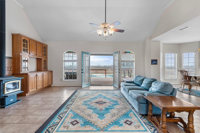 living area with visible vents, high vaulted ceiling, a ceiling fan, light tile patterned flooring, and a wood stove