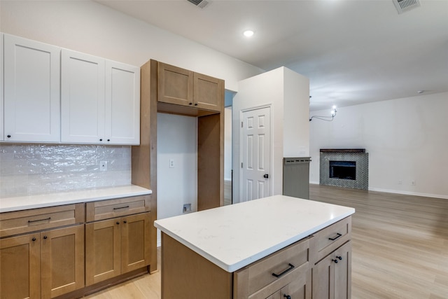 kitchen with visible vents, light wood finished floors, a tile fireplace, decorative backsplash, and light countertops