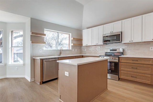 kitchen featuring a kitchen island, open shelves, a sink, light countertops, and appliances with stainless steel finishes