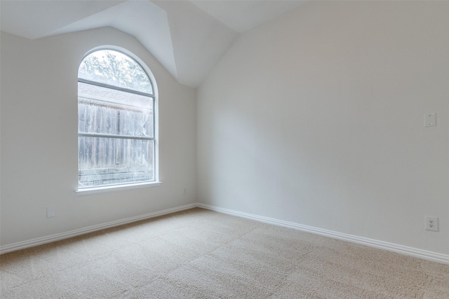 carpeted empty room featuring baseboards and vaulted ceiling