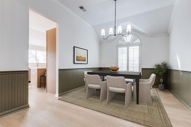 dining room featuring a wainscoted wall, visible vents, lofted ceiling, ornamental molding, and light wood-style floors