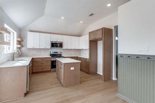 kitchen with visible vents, a kitchen island, lofted ceiling, appliances with stainless steel finishes, and a sink