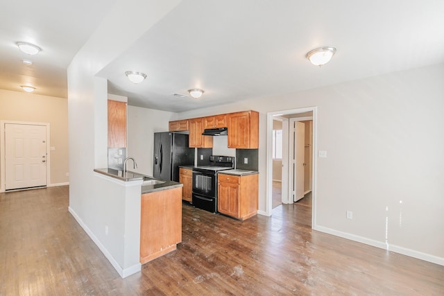 kitchen with dark wood-style floors, a peninsula, a sink, black appliances, and under cabinet range hood