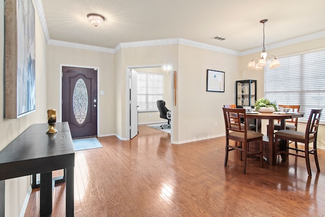 dining area featuring visible vents, wood finished floors, an inviting chandelier, crown molding, and baseboards