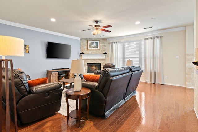 living area featuring a stone fireplace, crown molding, and wood finished floors