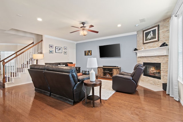 living area with wood finished floors, visible vents, a fireplace, stairs, and crown molding