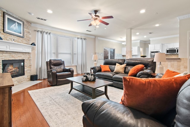 living room with crown molding, light wood-style flooring, a fireplace, and visible vents