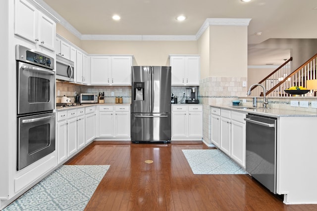 kitchen with dark wood-type flooring, a sink, stainless steel appliances, a peninsula, and crown molding