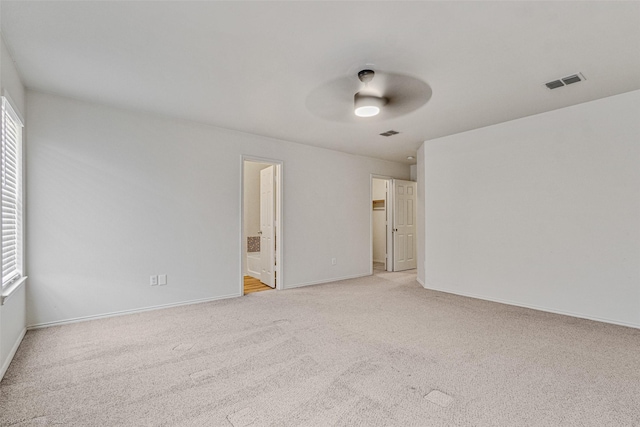 empty room featuring visible vents, light colored carpet, baseboards, and a ceiling fan