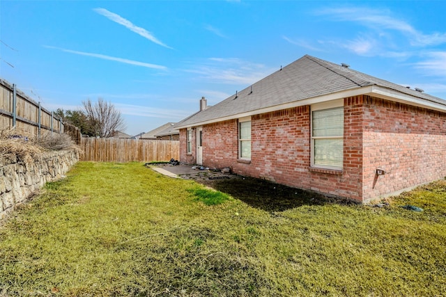 exterior space featuring a lawn, brick siding, a fenced backyard, and a chimney