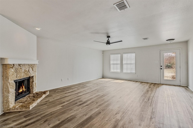 unfurnished living room featuring visible vents, plenty of natural light, a stone fireplace, and wood finished floors