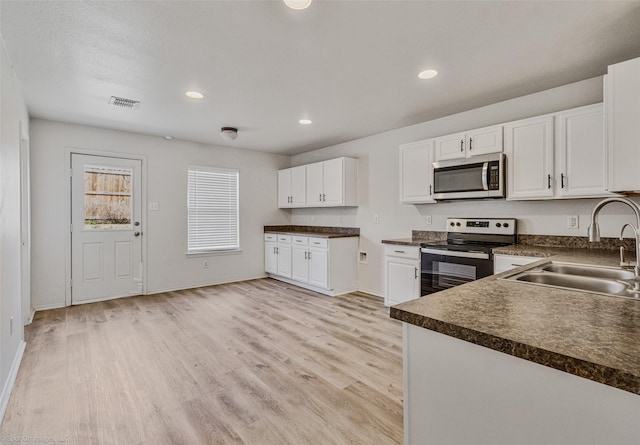 kitchen with visible vents, light wood finished floors, a sink, appliances with stainless steel finishes, and dark countertops