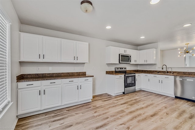 kitchen with dark countertops, white cabinets, stainless steel appliances, and light wood-style floors