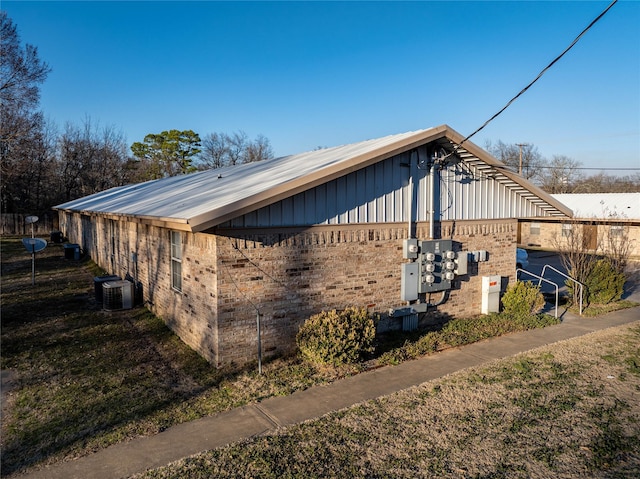 view of home's exterior with board and batten siding, brick siding, and central AC