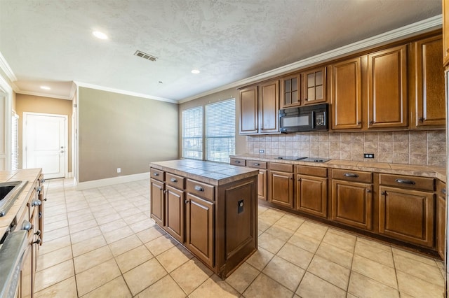 kitchen with tasteful backsplash, visible vents, crown molding, brown cabinetry, and black appliances