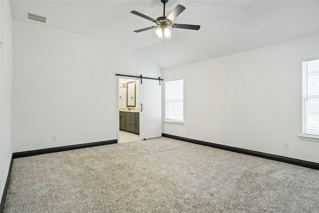 unfurnished bedroom with visible vents, baseboards, light colored carpet, a barn door, and vaulted ceiling