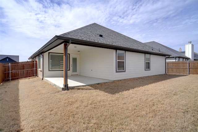 rear view of house with a yard, a patio area, a fenced backyard, and a shingled roof