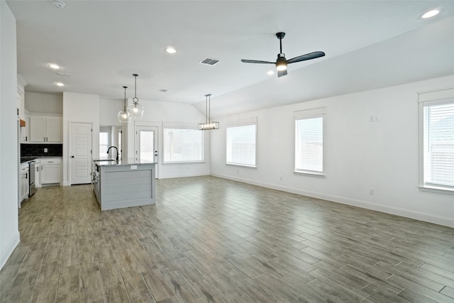 kitchen featuring tasteful backsplash, visible vents, a center island with sink, ceiling fan with notable chandelier, and wood finished floors