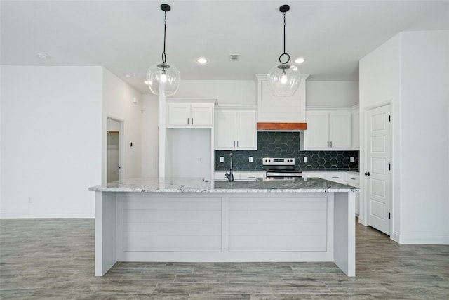 kitchen with premium range hood, stainless steel electric stove, a large island with sink, white cabinetry, and tasteful backsplash