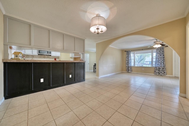 kitchen featuring stainless steel microwave, crown molding, light tile patterned flooring, arched walkways, and a ceiling fan