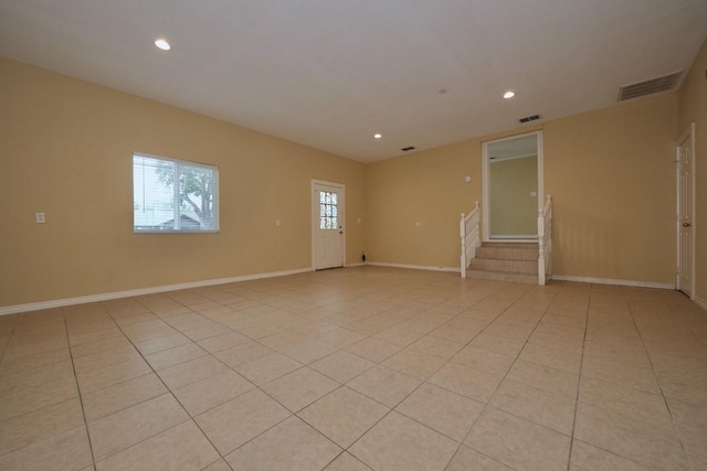 empty room featuring light tile patterned floors, visible vents, and stairway