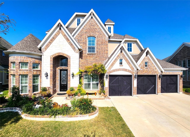 french country inspired facade featuring brick siding, an attached garage, a shingled roof, a front yard, and driveway