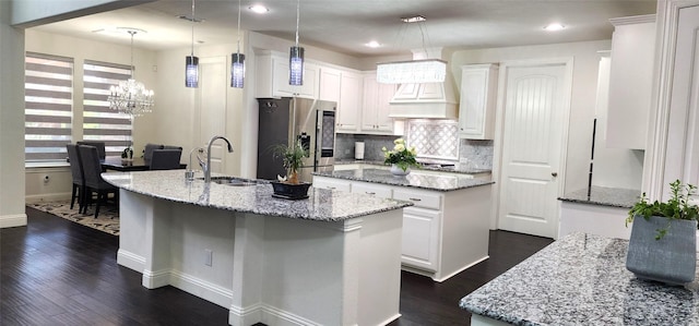 kitchen featuring dark wood-type flooring, an island with sink, stainless steel refrigerator with ice dispenser, and a sink