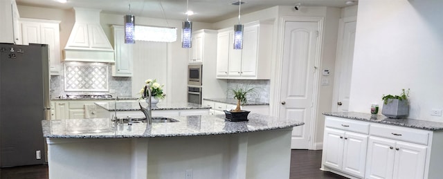 kitchen featuring an island with sink, custom exhaust hood, white cabinets, stainless steel appliances, and a sink